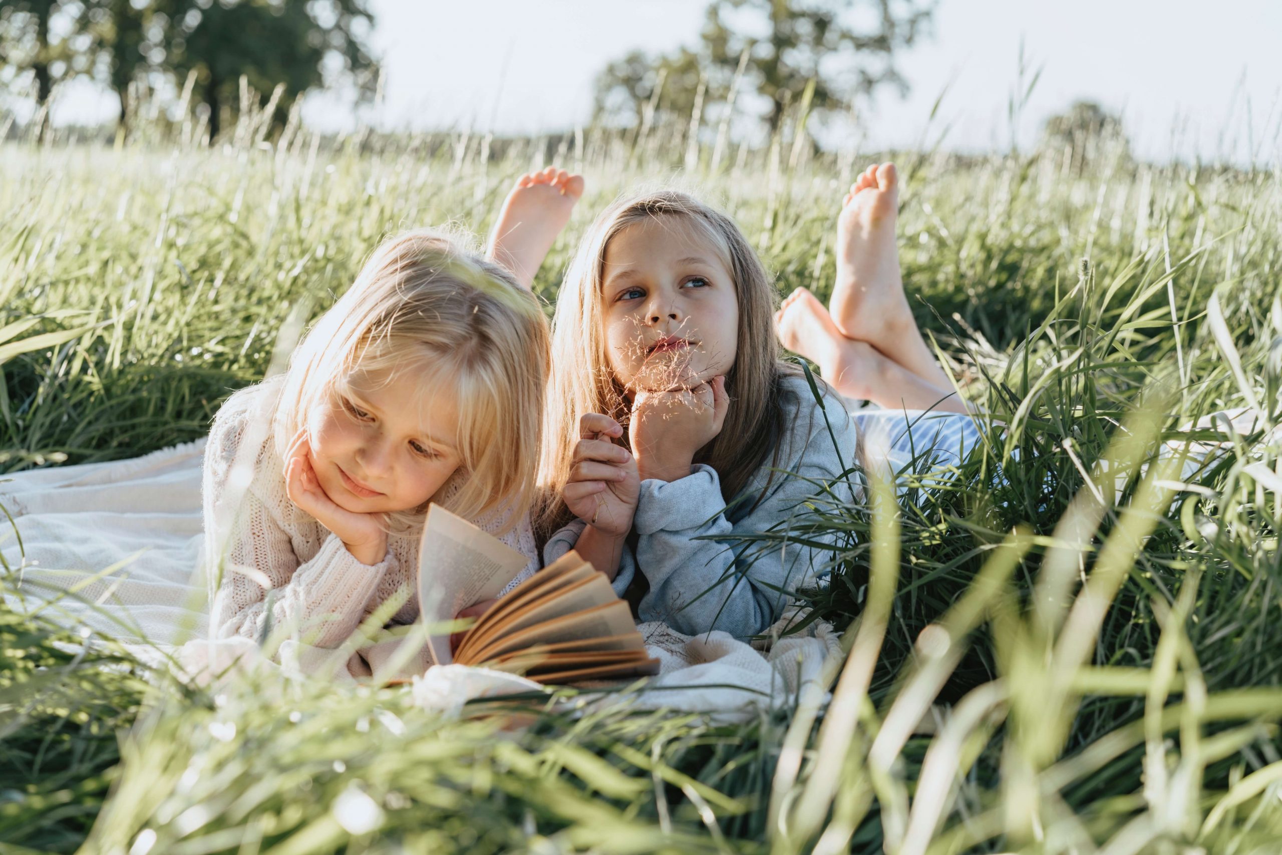 duas meninas crianças deitadas num relvado sobre uma manta a ler um livro